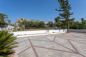 Ein Innenhof mit geometrischen Musterungen im Pflaster, Palmen und einem Berg im Hintergrund.