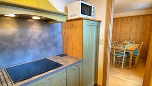 A compact kitchen with a built-in stove, a microwave, and a dining area with a wooden table and chairs. - Holiday Apartment Chalet Monteneve Toilà with Mountain View, Balcony & Wi-Fi (livigno)