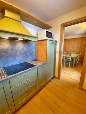 Una cocina compacta con estufa integrada, un microondas y un comedor con mesa y sillas de madera.