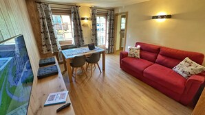 A room with a dining table, chairs, a red sofa, and a TV. - Holiday Apartment Chalet Monteneve Toilà with Mountain View, Balcony & Wi-Fi (livigno)