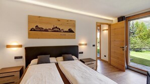 A bedroom with a bed, bedside tables, a wooden headboard, a cityscape artwork, and a sliding glass door leading to a garden. - Holiday Apartment Chalet Monteneve Neve with Mountain View, Shared Garden & Wi-Fi (Livigno)