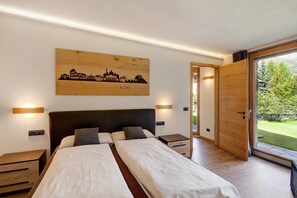 Camera da letto con un letto, comodini, una testiera in legno, un'opera d'arte con una veduta cittadina e una porta a vetri scorrevoli che dà su un giardino.