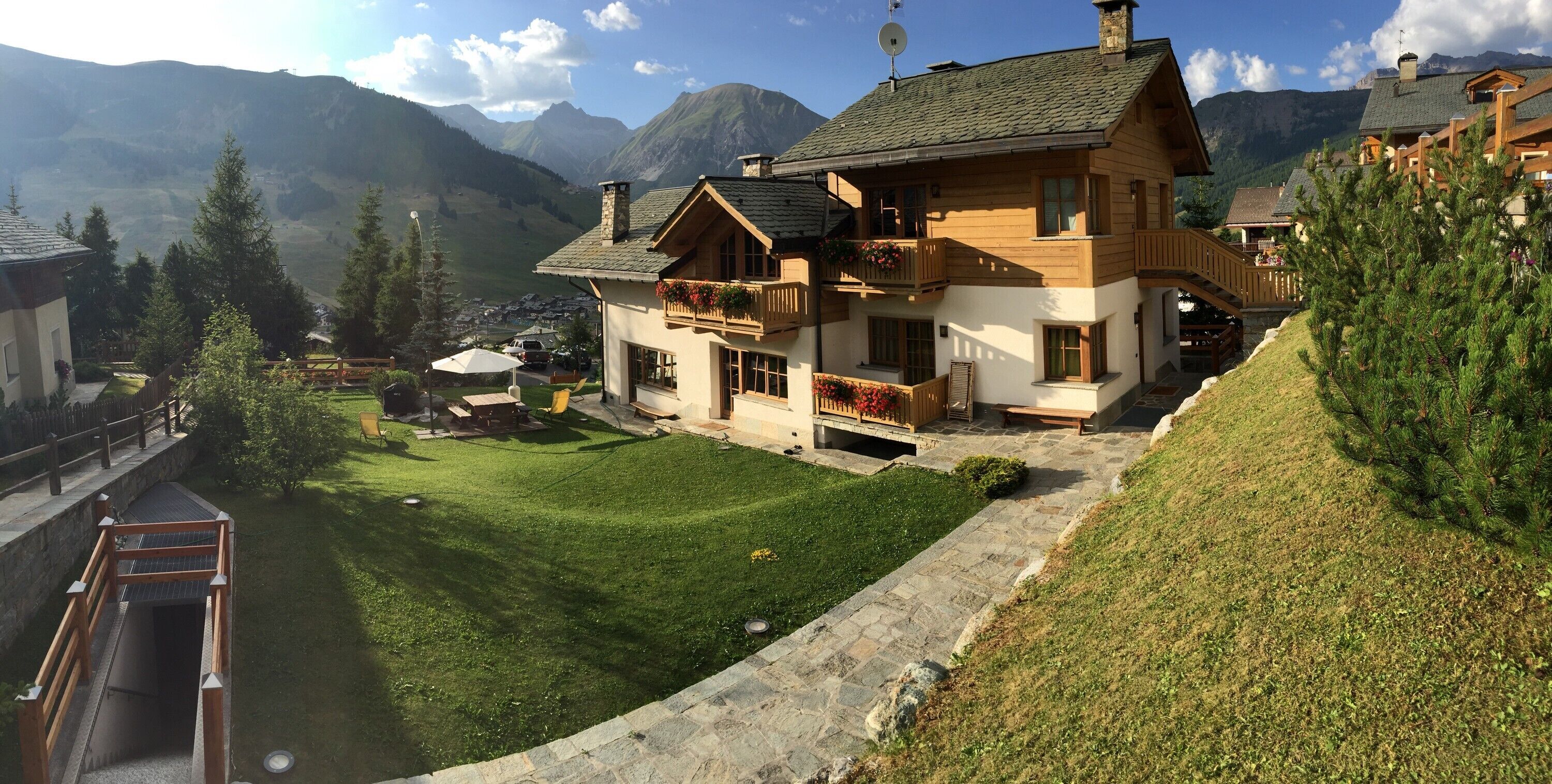A chalet with a balcony, a stone pathway, and a view of mountains.