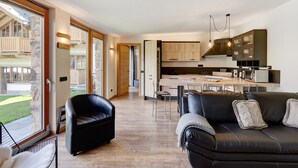 A modern living room with a black leather sofa and a dining area with a wooden table and chairs. - Holiday Apartment Chalet Monteneve Neve with Mountain View, Shared Garden & Wi-Fi (Livigno)
