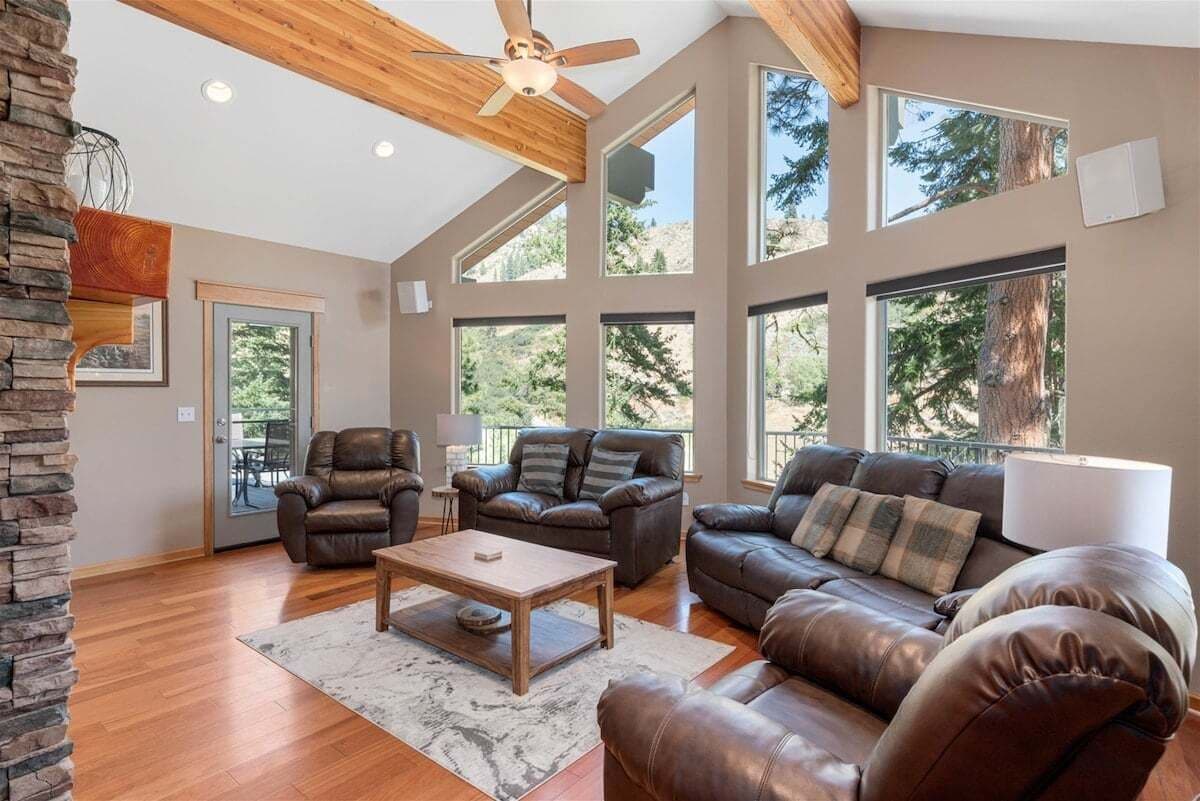 Ein großzügiges Wohnzimmer mit Ledersofas, einem Holztisch und großen Fenstern mit Blick auf Bäume.