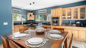 Een keuken met houten kastjes, een eettafel gedekt met borden en glazen, en een bordje met de tekst 'home' aan de muur.