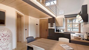 Una cocina moderna con encimera de madera, una mesa de comedor y sillas. Se observa un microondas, una tetera y una ventana que proporciona luz natural.