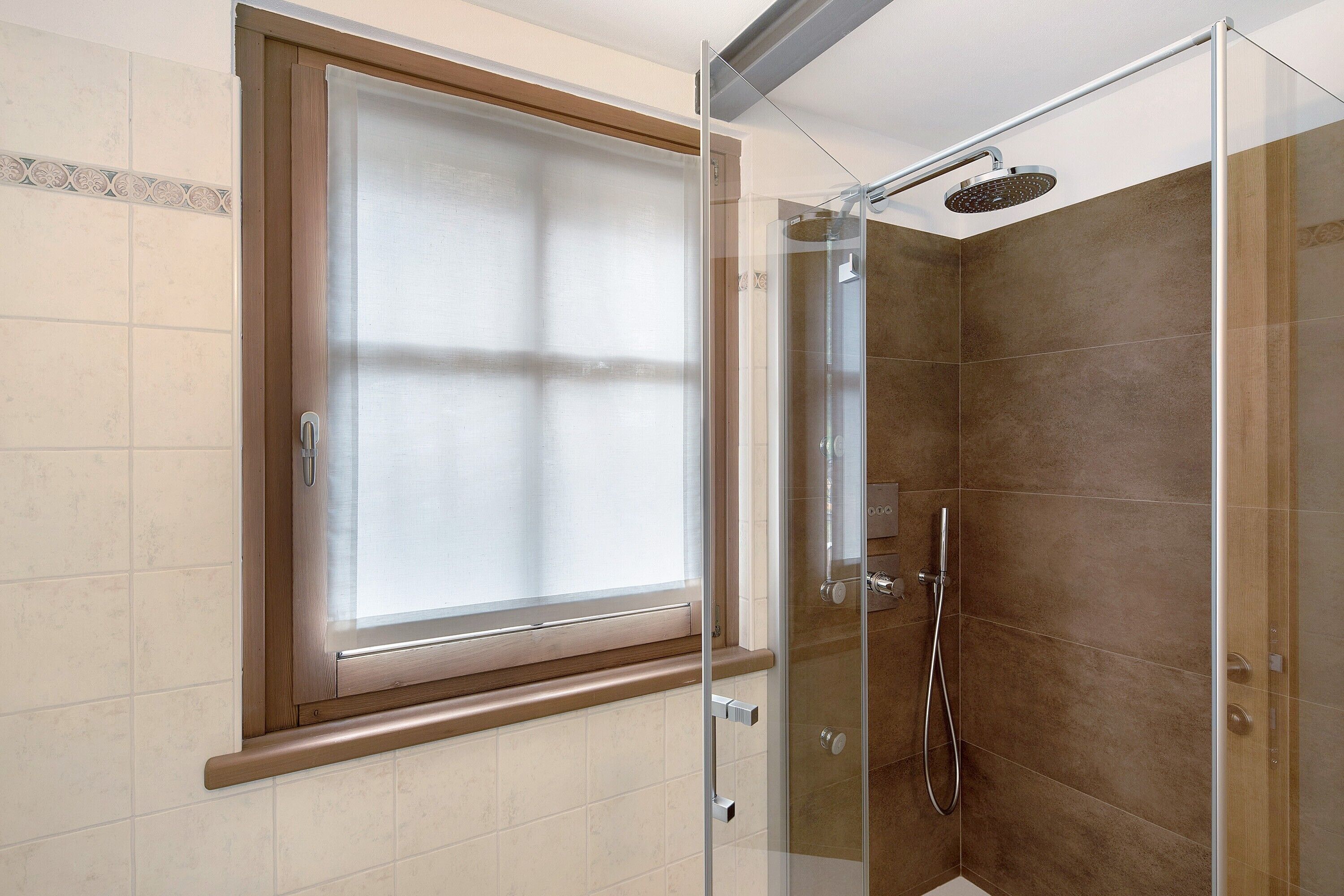 A shower with a glass door, a window above it, and a showerhead.