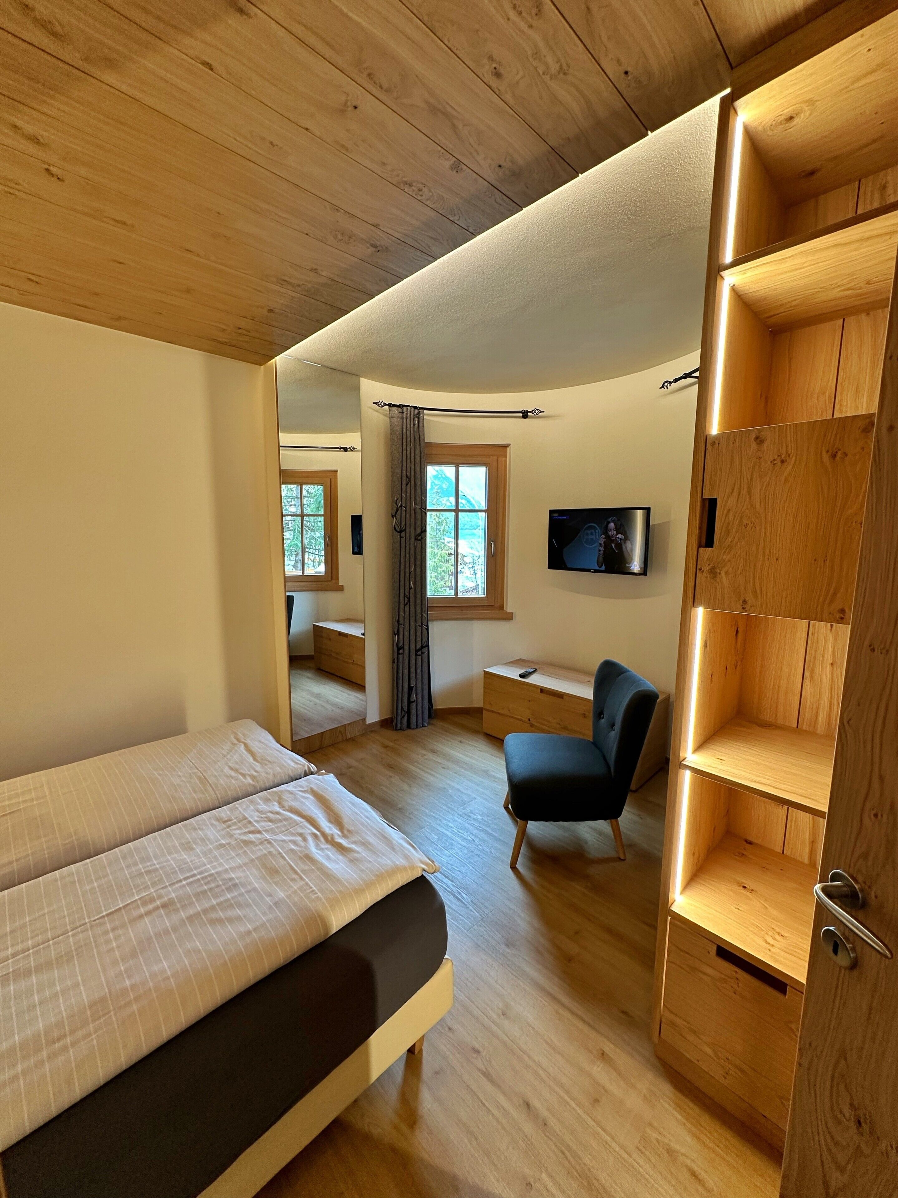 A bedroom with a bed, a chair, a TV, and a wooden shelf unit.