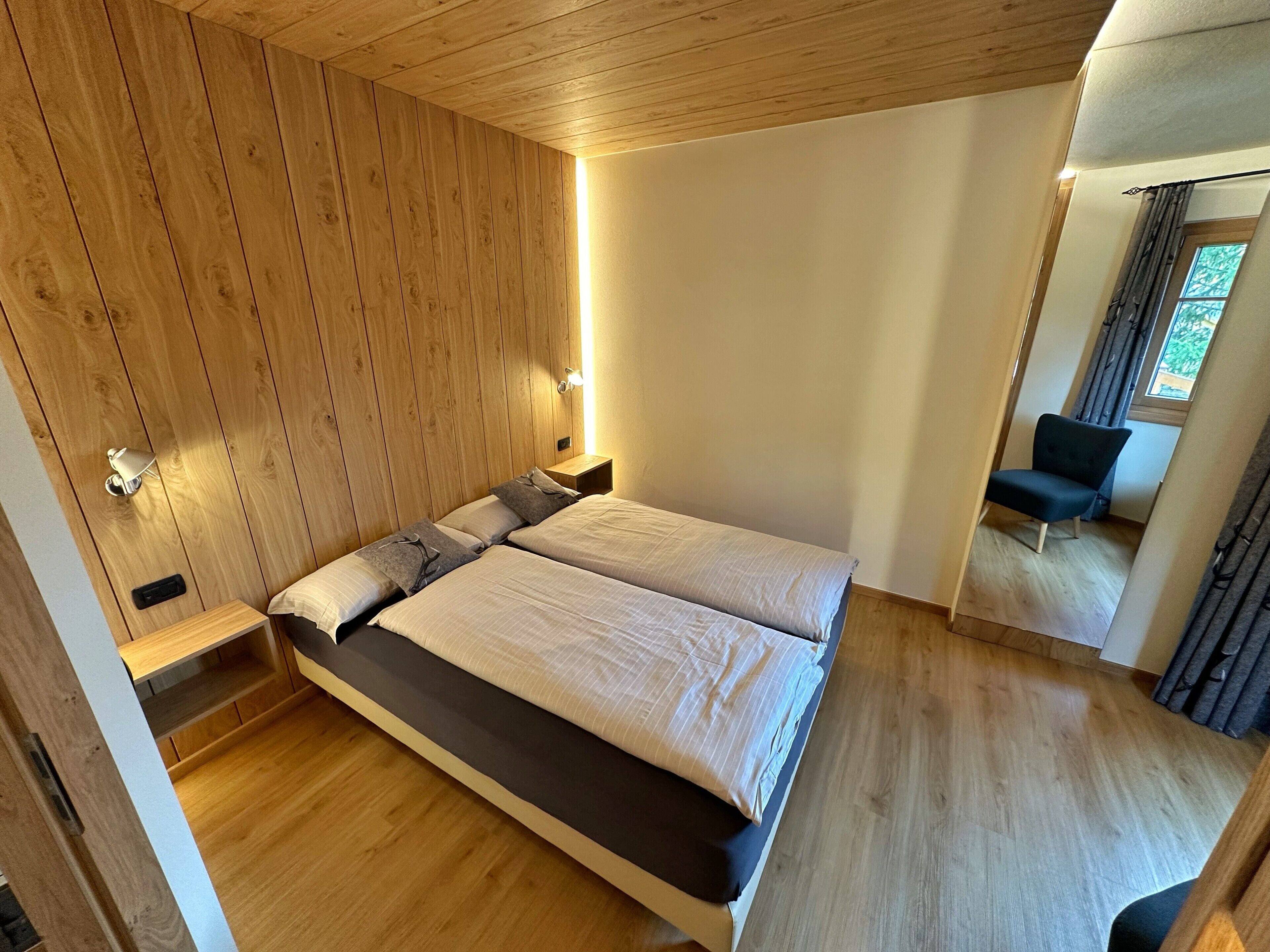 Ein modernes Schlafzimmer mit Holzboden, einem großen Bett mit weißer und dunkler Bettwäsche, einem Nachttisch und einem Sessel.