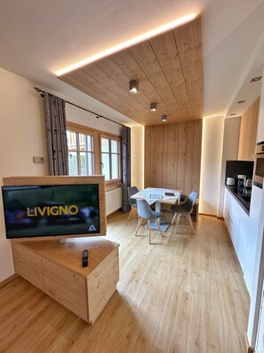 Un espace de vie moderne doté d’un téléviseur à écran plat, de planchers en bois, d’un coin repas et d’une cuisine.