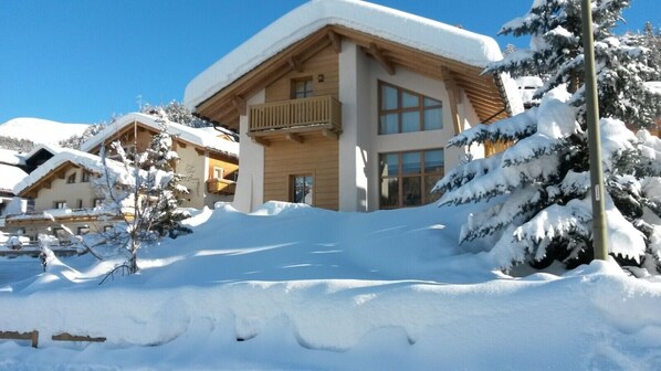 Un bâtiment recouvert de neige, doté d’un balcon, et entouré d’arbres chargés de neige.