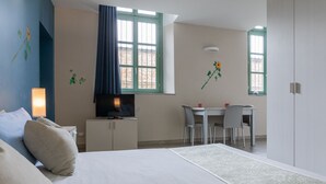 A bedroom with a bed, a TV, a desk, and two chairs. - Housing Giulia - Studio 2/4 by Wonderful Italy (Torino)