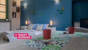 A modern bedroom with a blue accent wall, a bed with white bedding, two bedside tables with lamps, a coffee table with a colorful table runner, and a red mug. - Housing Giulia - Studio 2/4 by Wonderful Italy (Torino)