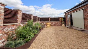 Une cour avec un chemin de gravier, des murs en briques, des clôtures en bois et un petit jardin agrémenté de plantes et de fleurs.