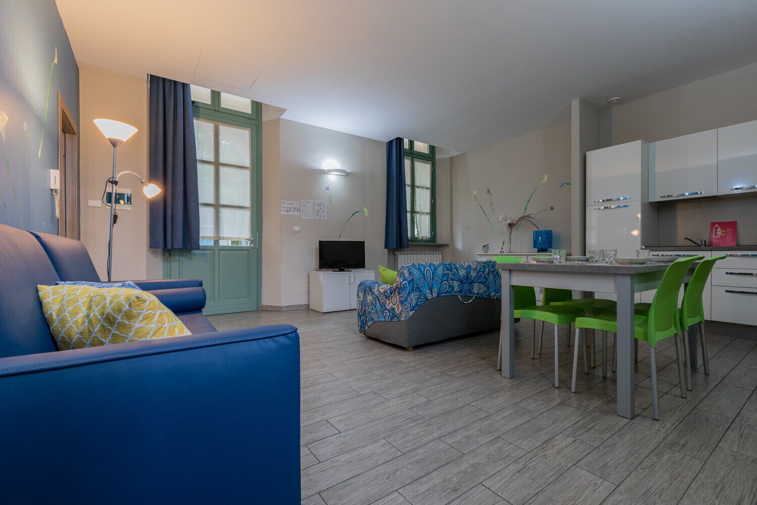 Ein modernes Wohnzimmer mit einer Couch, einem Esstisch mit Stühlen, einem Fernseher und einer Küchenzeile.
