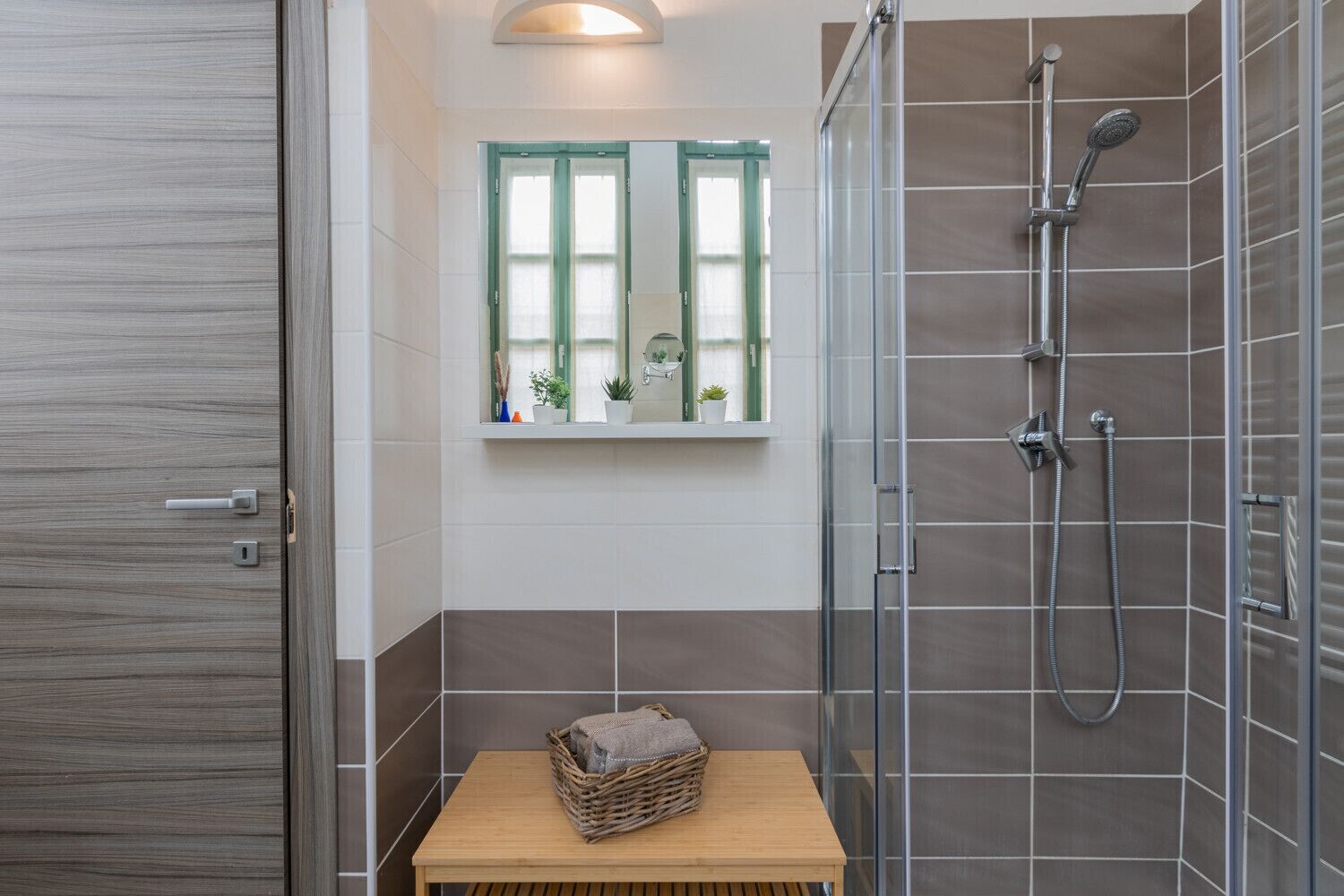 Ein modernes Badezimmer mit Duschkabine aus Glas, einem kleinen Fenster mit Ausblick und einer hölzernen Bank mit Korb.