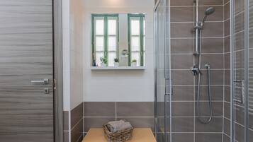 Ein modernes Badezimmer mit Duschkabine aus Glas, einem kleinen Fenster mit Ausblick und einer hölzernen Bank mit Korb.