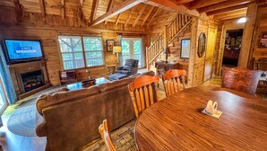 A cozy log cabin interior with a fireplace, wooden furniture, and a television. - Breezy River Cabin | Mountain Views, Hot Tub, Game Room & River Access (Piney Creek)