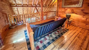 A wooden cabin interior with a loft bedroom, a wooden staircase, and a checkered rug. - Breezy River Cabin | Mountain Views, Hot Tub, Game Room & River Access (Piney Creek)