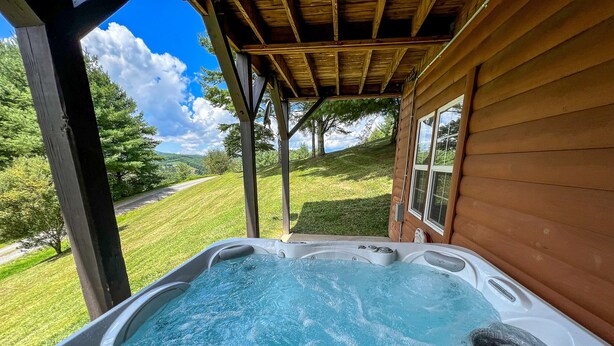 A hot tub with a wooden deck and a view of a grassy landscape. - Breezy River Cabin | Mountain Views, Hot Tub, Game Room & River Access (Piney Creek)
