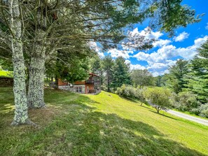 Une cabane aux murs en pierre, entourée d’une végétation luxuriante et d’arbres.
