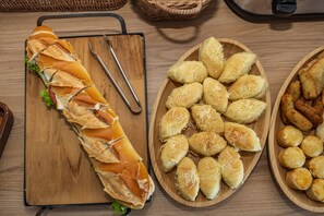 A wooden cutting board with a sliced sandwich and two wooden plates with bread rolls.