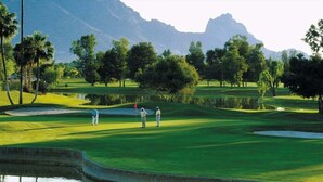 En golfbane med et vandhazard, træer og bjerge i baggrunden.
