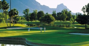 Ein Golfplatz mit einem Wasserschutzgebiet, Bäumen und Bergen im Hintergrund.