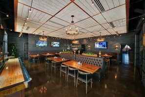 Ein Restaurant mit Barbereich, Sitzboxen und einer hohen Decke mit freiliegenden Balken und Leuchten.