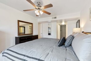 Ein Schlafzimmer mit einem großen Bett, einem Deckenventilator, einem Spiegel und einer Tür zu einem anderen Raum.