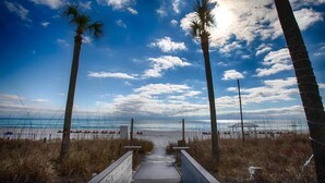 A wooden pathway leading to a beach with palm trees and a clear sky. - Beachfront! Lg Balcony Amazing Gulf-Beach Views! (Panama City Beach)
