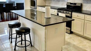 Cocina moderna con armarios blancos, una isla central con taburetes, electrodomésticos de acero inoxidable y vistas a un comedor.