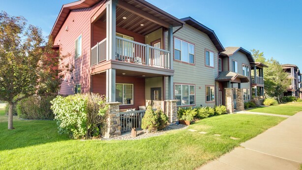 A two-story residential building with a balcony, stone pillars, and a well-maintained lawn. - Cozy Livingston Condo w/ Balcony & Mtn View! (Livingston)