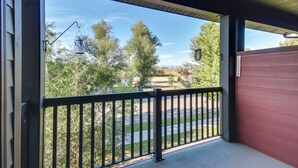A covered balcony with a metal railing, a view of a street, and trees in the background. - Cozy Livingston Condo w/ Balcony & Mtn View! (Livingston)