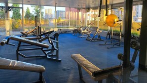 Ett gym med träningsutrustning, stora fönster och utsikt över byggnader.