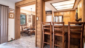 A wooden interior with a kitchen area featuring a refrigerator, a microwave, and wooden cabinets. There is a dining table with chairs and a chandelier. - Elkhorn Bluff Condo with Community & Resort Amenities (Sun Valley)
