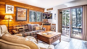 A cozy living room with a plaid sofa, a wooden coffee table, and a television. There are framed pictures on the wall and a sign that reads "Welcome to the Mountains." - Elkhorn Bluff Condo with Community & Resort Amenities (Sun Valley)