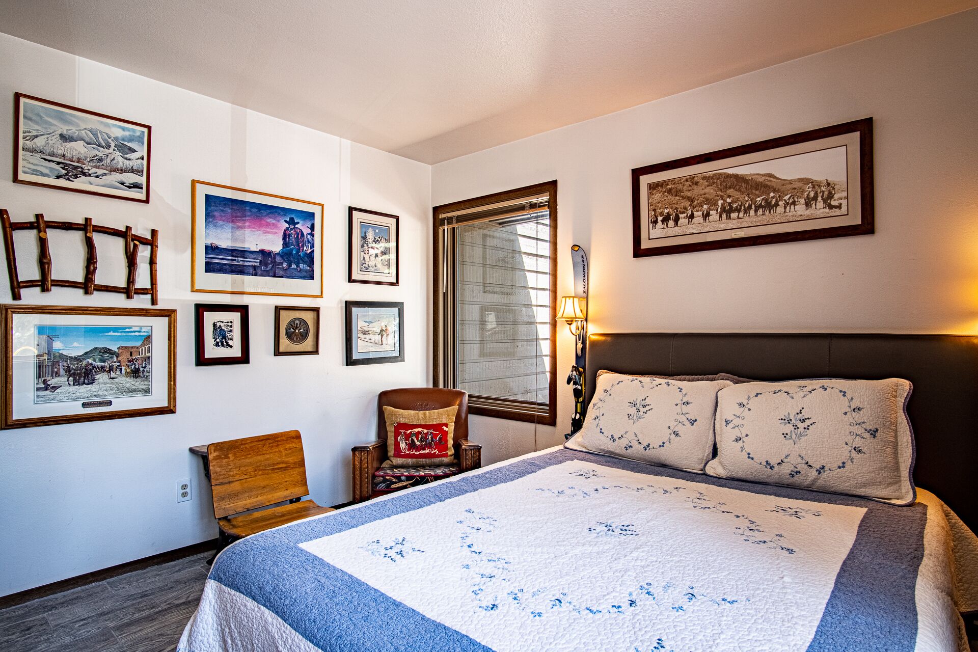 Une chambre d’hôtel avec un grand lit, une chaise en bois, une petite table et plusieurs tableaux encadrés accrochés aux murs.