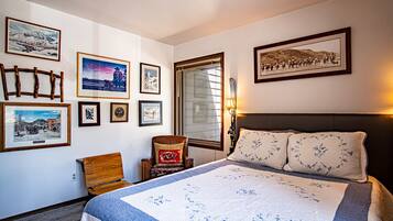 Une chambre d’hôtel avec un grand lit, une chaise en bois, une petite table et plusieurs tableaux encadrés accrochés aux murs.