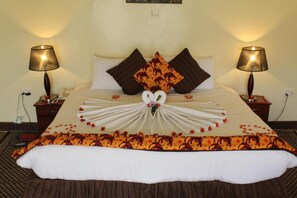 Una cama bien hecha con un arreglo decorativo de toallas en el centro, dos lámparas de noche y una colcha estampada.