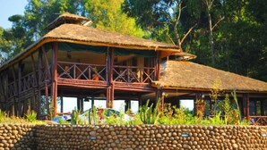 A rustic building with a thatched roof, wooden beams, and a stone wall in front. - Da Vinci Gorilla Lodge (Muhoza)