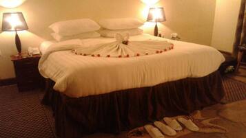 A neatly made bed with a decorative towel arrangement, two bedside lamps, and a small bedside table with a phone and a glass.