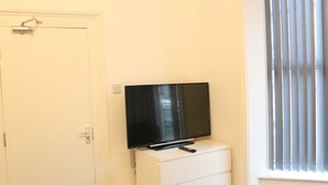 A room with a television on a white dresser, a door, and a window with blinds. - St. Peter's Shared House (Birmingham)