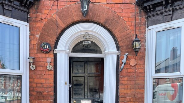 A brick building with a black door, white trim, and a welcome sign. - St. Peter's Shared House (Birmingham)
