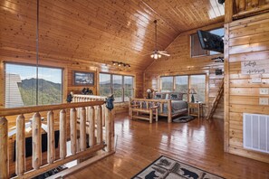 A wooden cabin interior with a bed, a desk, and a view of the mountains through large windows. - Luxurious Cabin|Majestic Views|Arcade|Hot Tub (Sevierville)