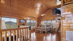 A wooden cabin interior with a bed, a desk, and a view of the mountains through large windows. - Luxurious Cabin|Majestic Views|Arcade|Hot Tub (Sevierville)