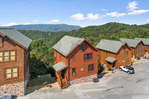 A row of log cabins with stone foundations, a paved driveway, and a vehicle parked in front. - Luxurious Cabin|Majestic Views|Arcade|Hot Tub (Sevierville)