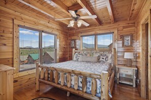 Un dormitorio tipo cabaña de madera con una cama, una mesita de noche, una lámpara y un ventilador de techo.