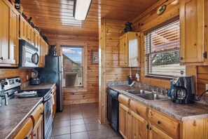 Cocina de cabaña de madera con estufa, refrigerador y ventana con persianas.